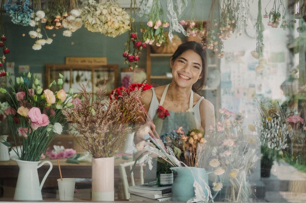 A florist smiling behind her shop window, surrounded by flowers